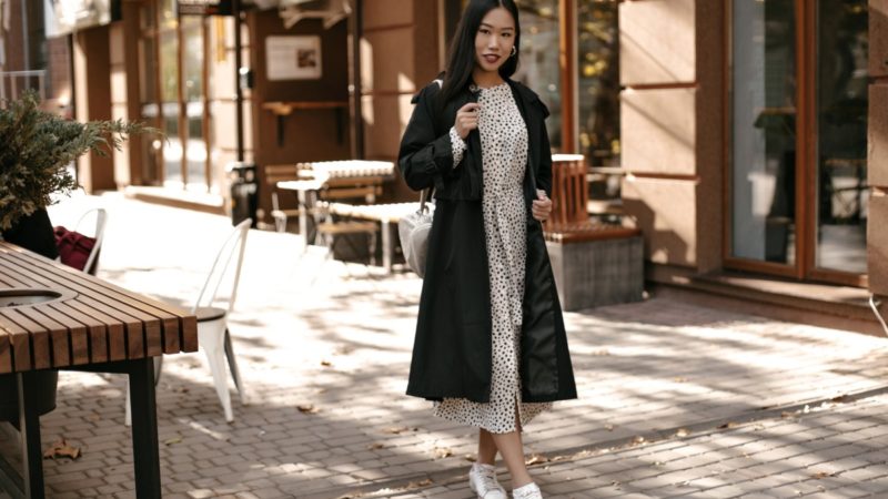 fulllength portrait brunette asian woman midi white dress black trench coat stands outside near street cafe 1